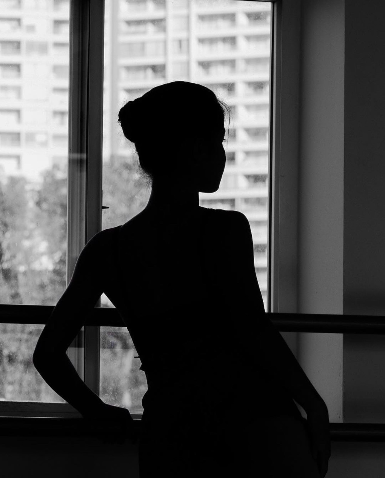 Silueta de una bailarina junto a la barra, frente a una ventana