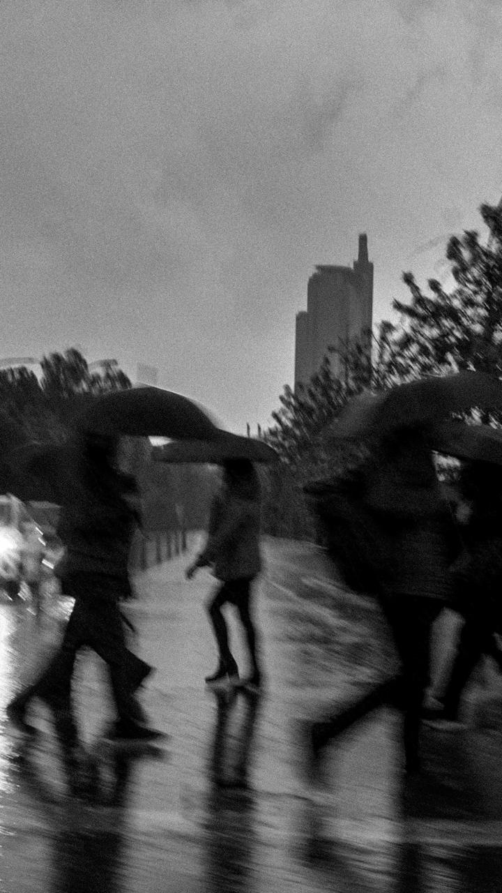 Personas con paraguas cruzando la calle bajo la lluvia, con una torre alta al fondo
