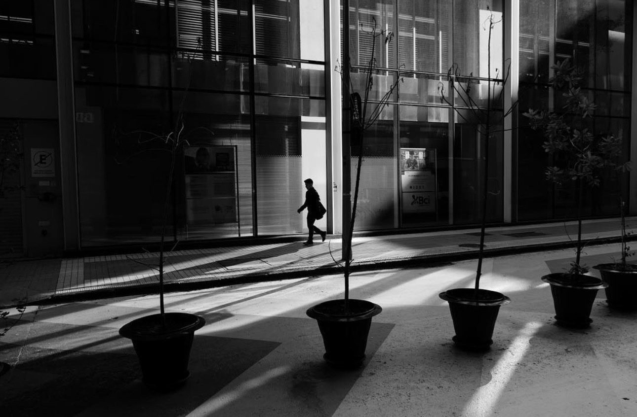 Un hombre en silueta cruzando frente a la fachada de cristal de un edificio, entre maceteros