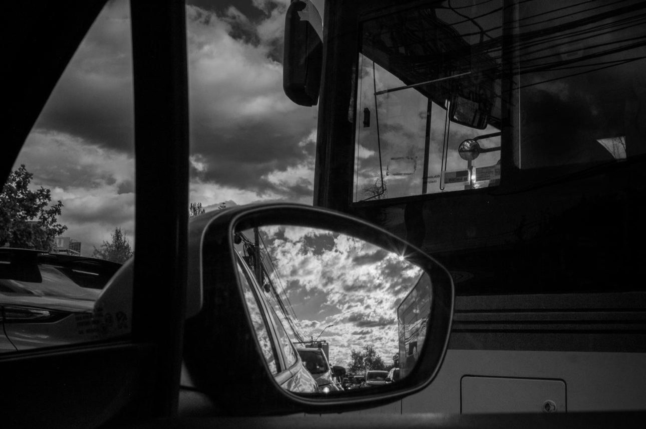 Espejo retrovisor reflejando el cielo nublado y el tráfico a sus espaldas