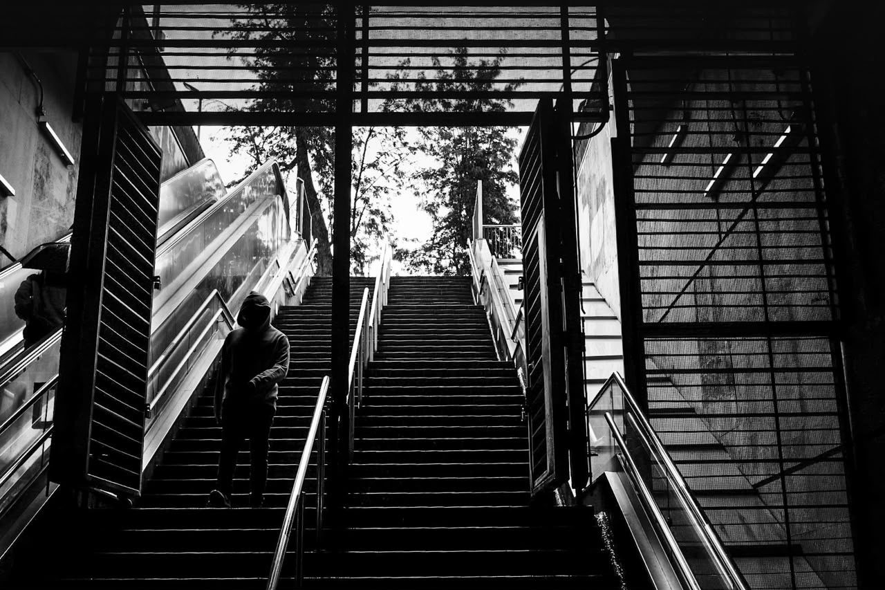 Una figura con capucha bajando las escaleras de una estación de metro, hacia la luz
