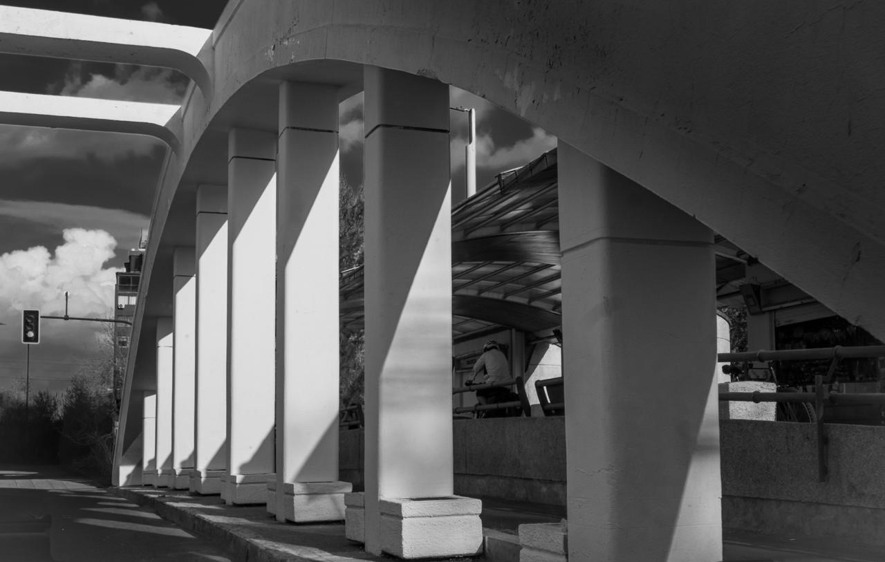 Una fila de pilares blancos bajo la estructura elevada, rayados por la luz en diagonal