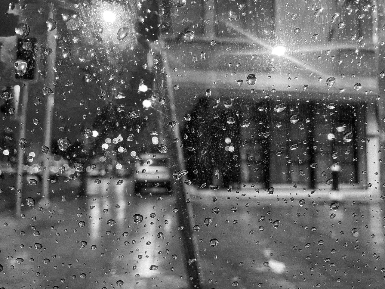 La calle de noche a través del parabrisas con gotas, con las luces de la ciudad desenfocadas