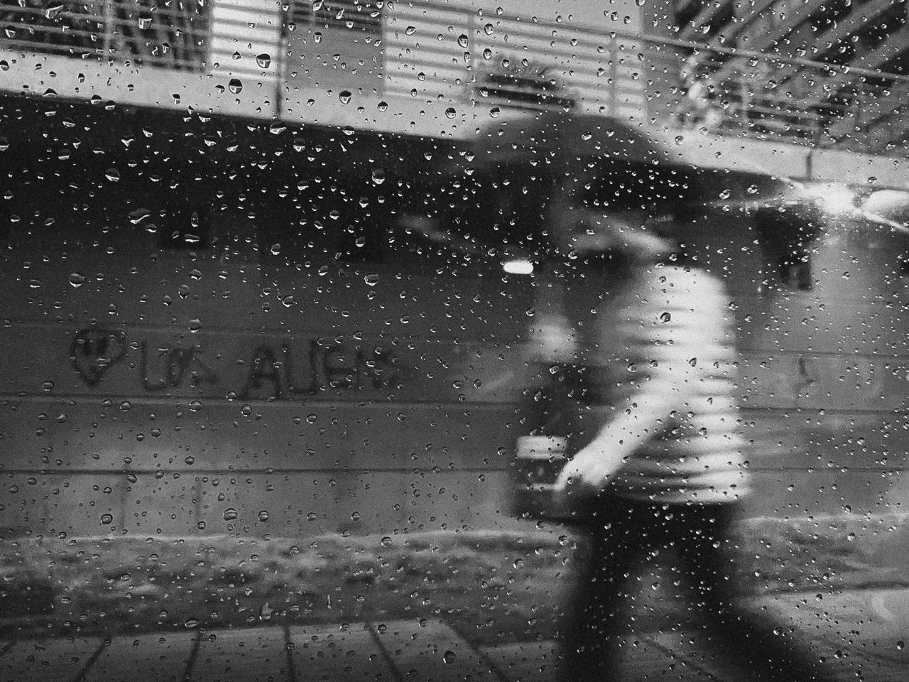 Un peatón con paraguas, borroso, visto a través de un vidrio cubierto de gotas de lluvia